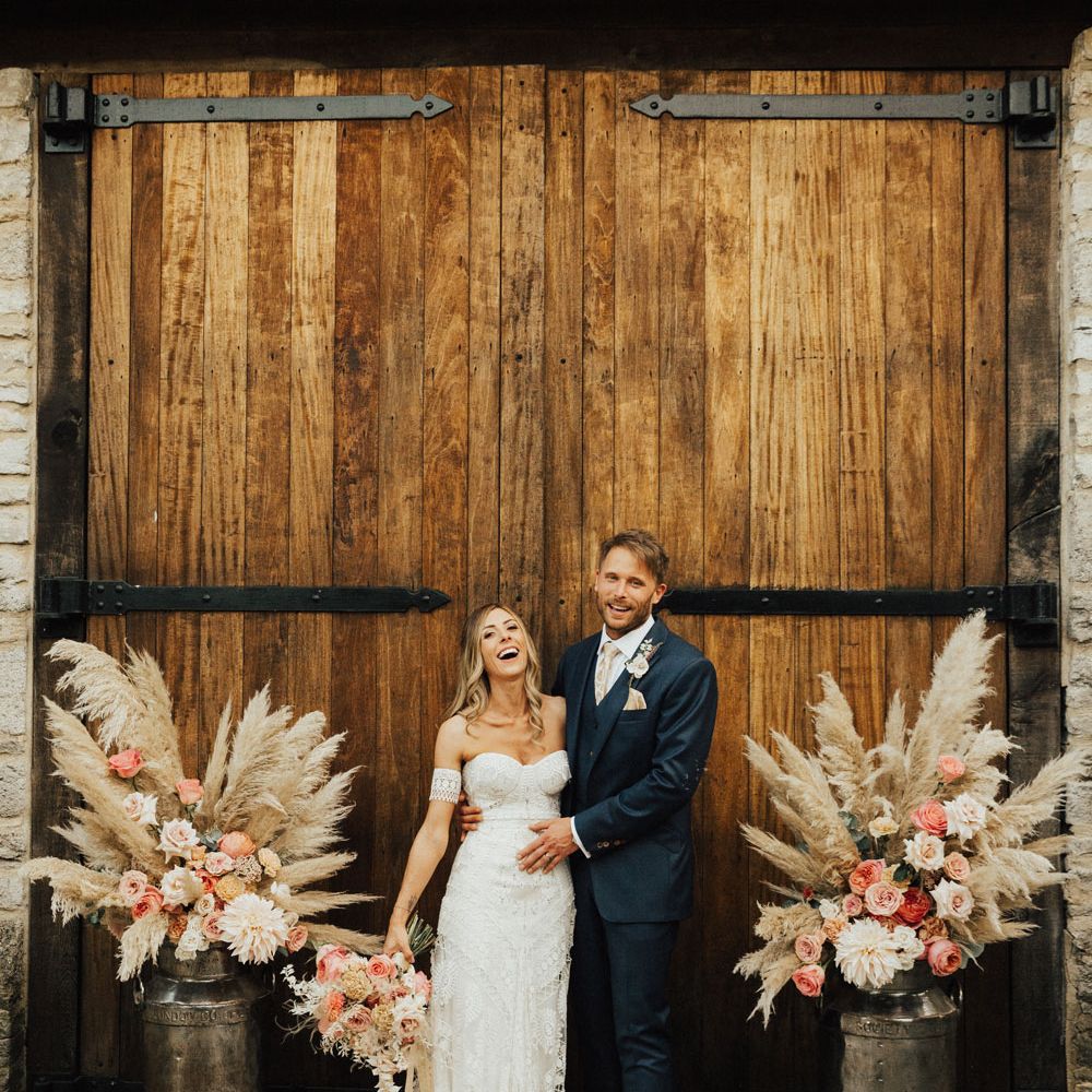 Bride and Groom stand between pampas grass and rose floral arrangements at Tythe Barn Wedding with boho decor