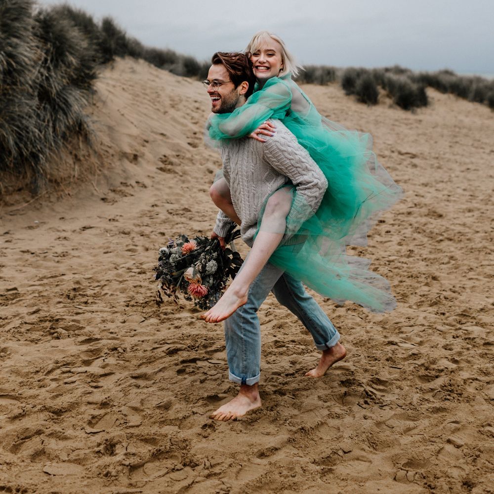 Bride in a sheer green wedding dress having a piggy back from her groom in jumper and jeans 
