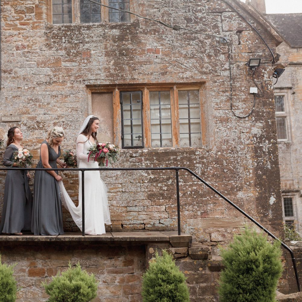 Bride with bridesmaids walking down steps outdoors at Brympton House