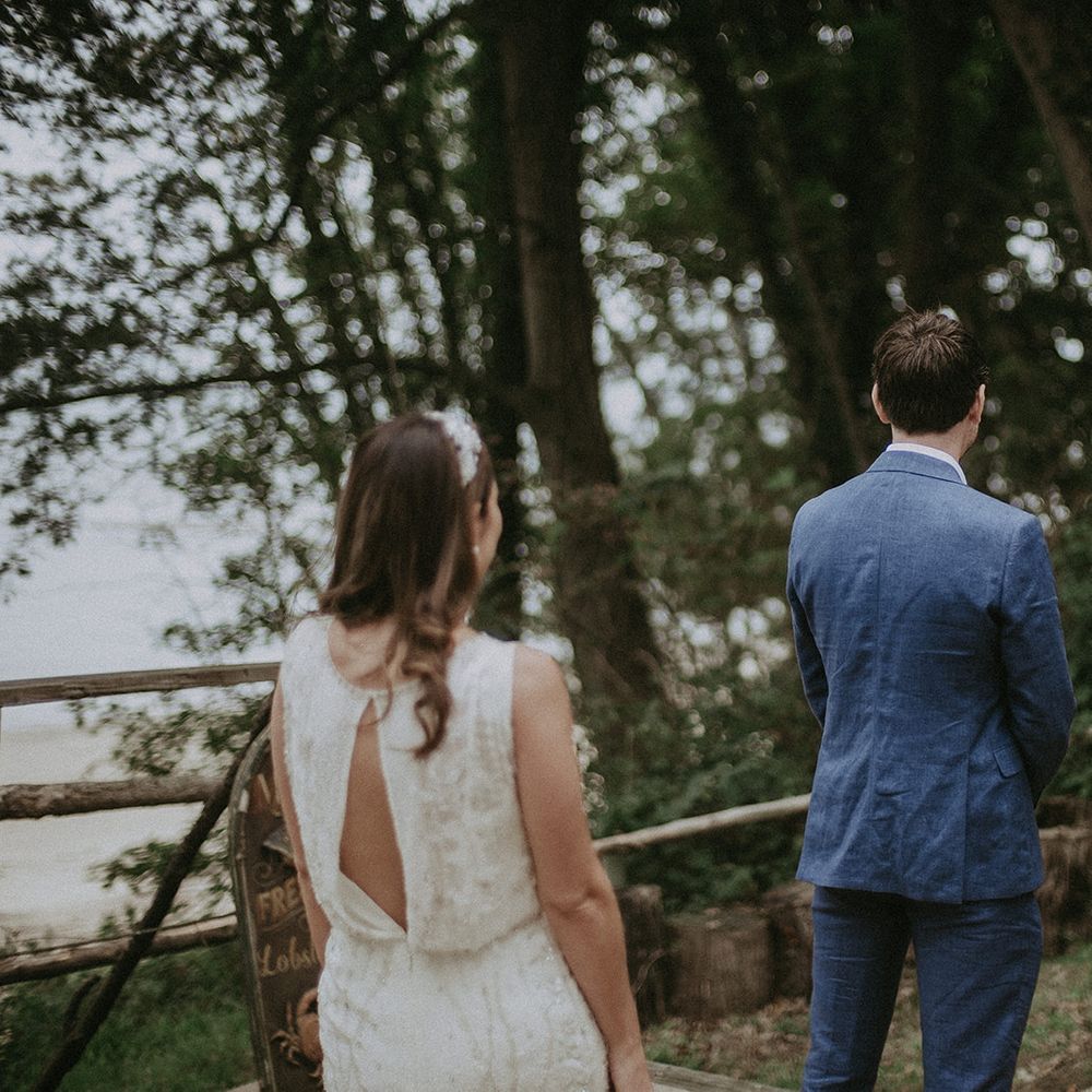 Bride stands behind groom as she waits for first look moment to be captured