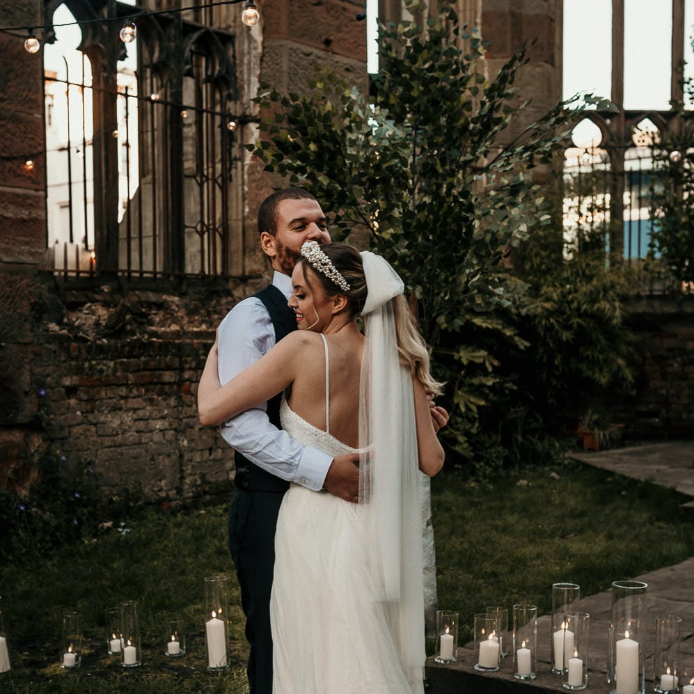 Groom embracing his bride in a bow veil surrounded by pillar candles at a bombed out church in Liverpool 
