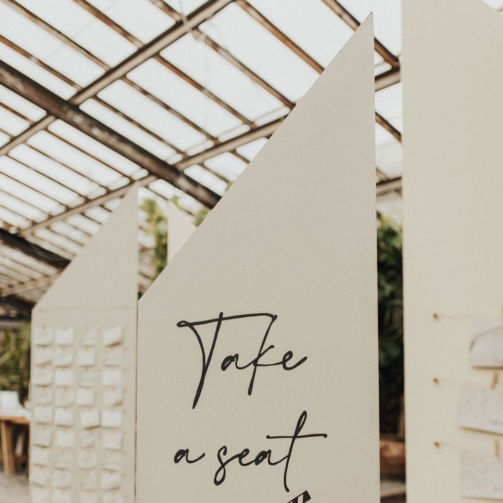 White angular wedding signs with black text and movie themed seating plan for glasshouse wedding breakfast at Anran Devon