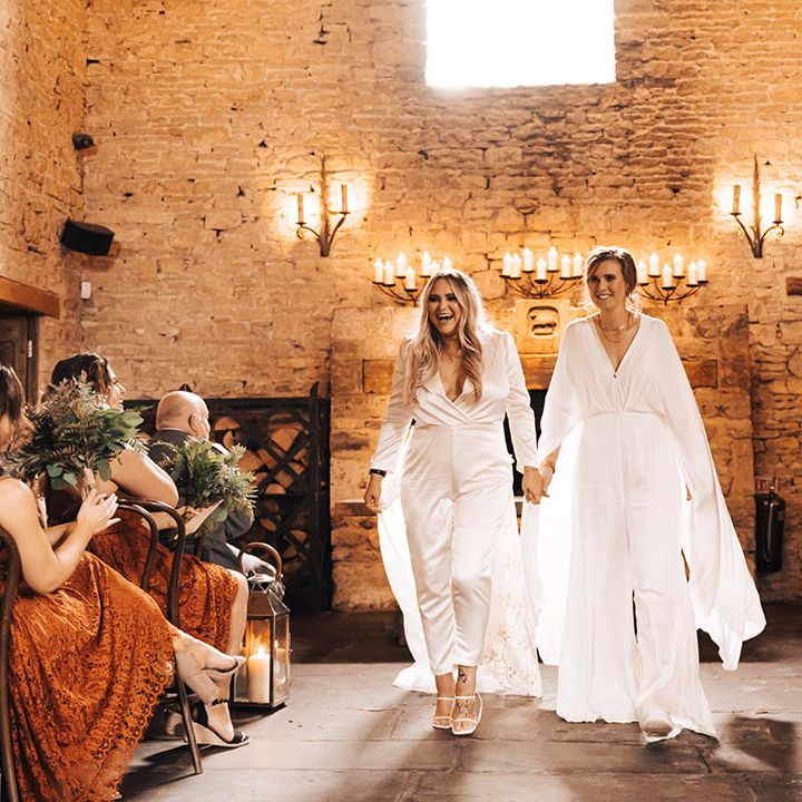 Brides hold hands and walk down the aisle with one another on their wedding day