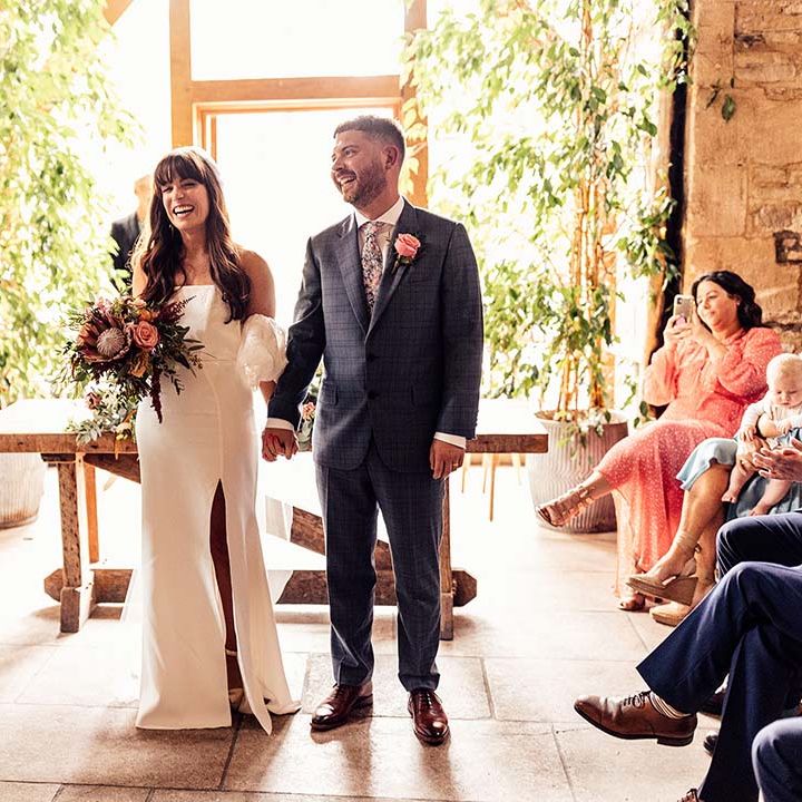 Bride & groom laugh as they hold hands with one another after wedding ceremony at the Stone Barn Cotswolds 