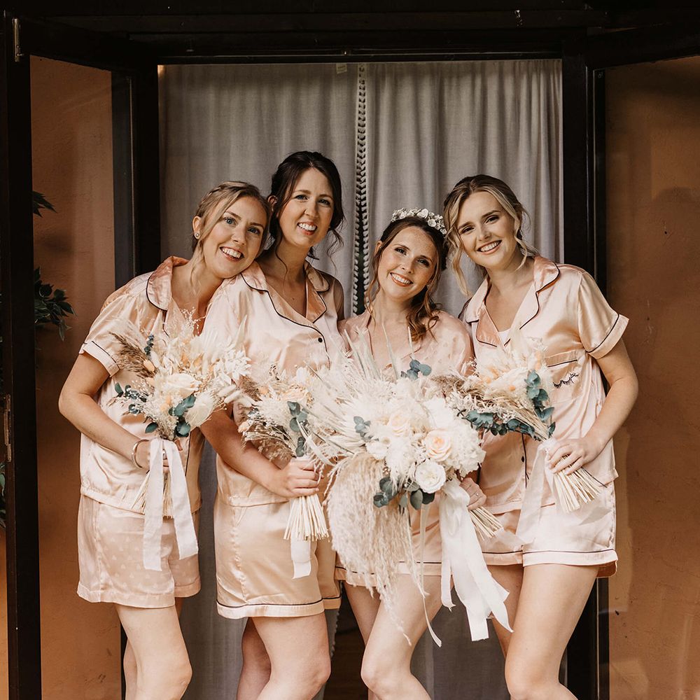 Bride stands with her bridesmaids on the morning of her wedding day as they all wear matching silk pyjamas