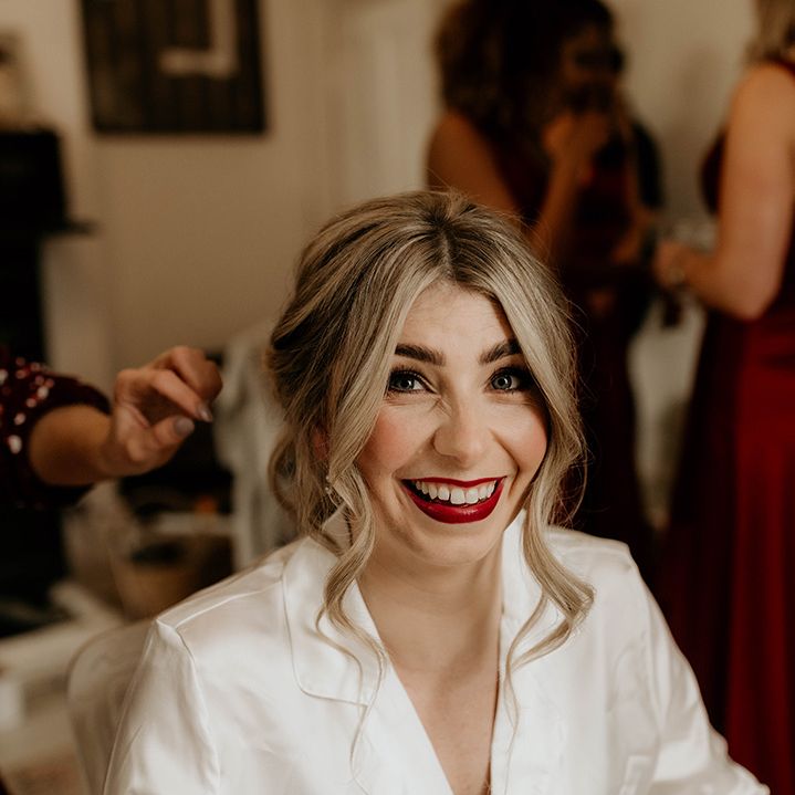 Bride in white satin pyjamas on her wedding morning with bright red lipstick 