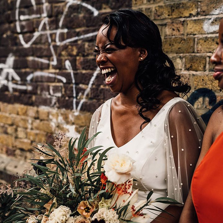 Beautiful black bride in a pearl top laughing with her bridesmaid in a burnt orange dress