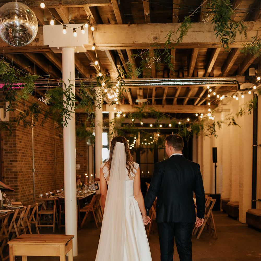 Bride and groom walk into 100 Barrington wedding venue with vines and fairy lights