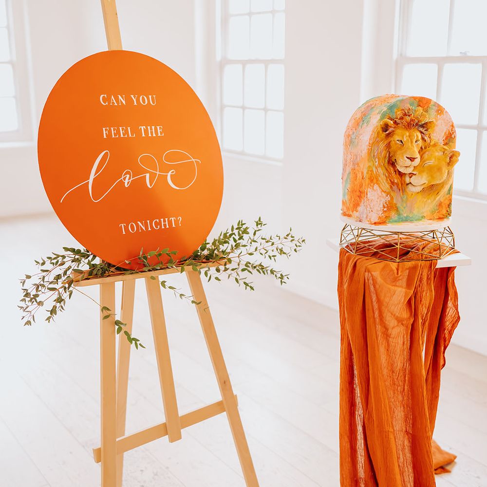 Orange can you feel the love tonight wedding sign and lion design wedding cake design on a gold and marble cake stand 
