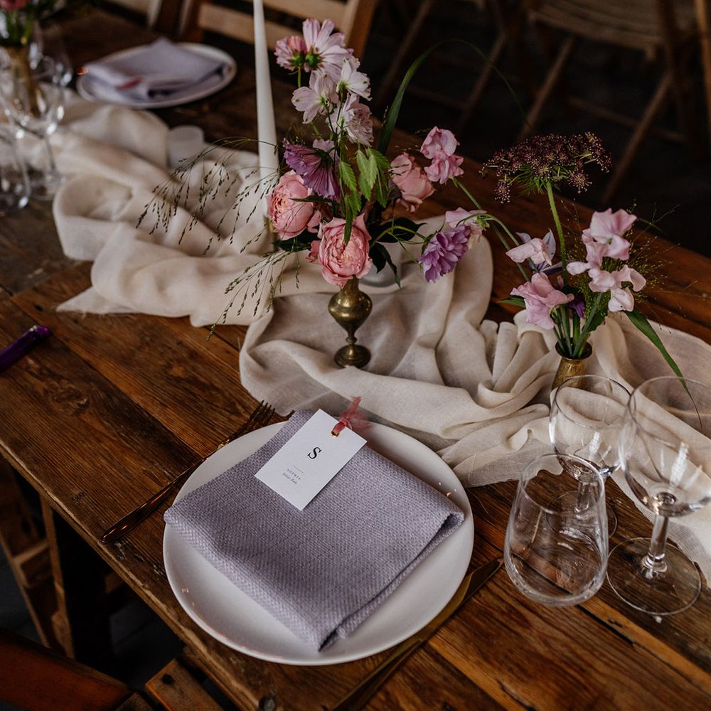 Place setting with lilac napkin and pink and white flowers stems in gold vessels 