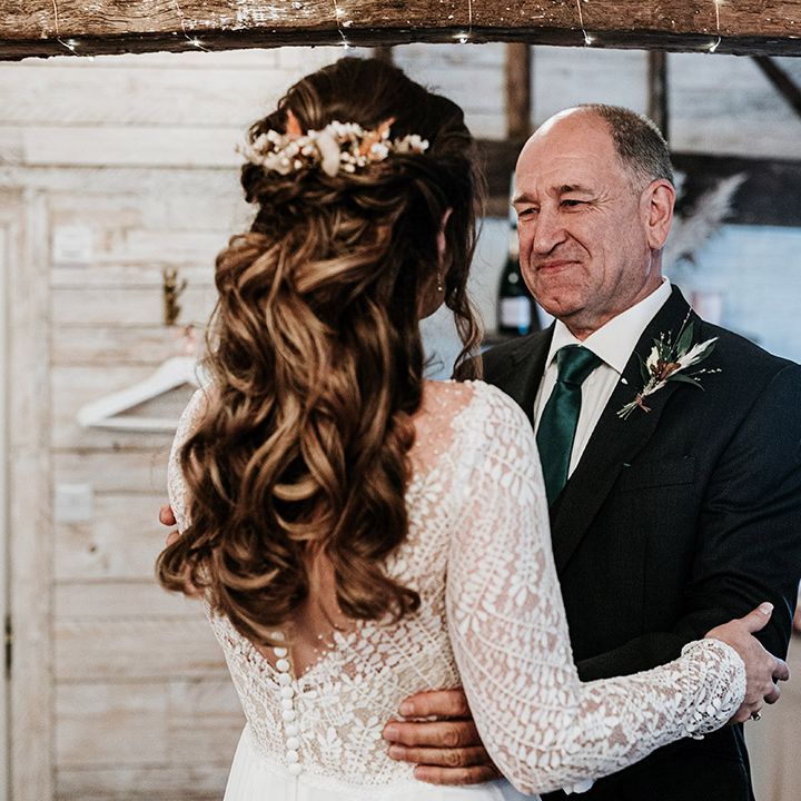 Father of the bride in black suit and emerald green tie smiles at the bride in long sleeve patterned dress with half up half down hair