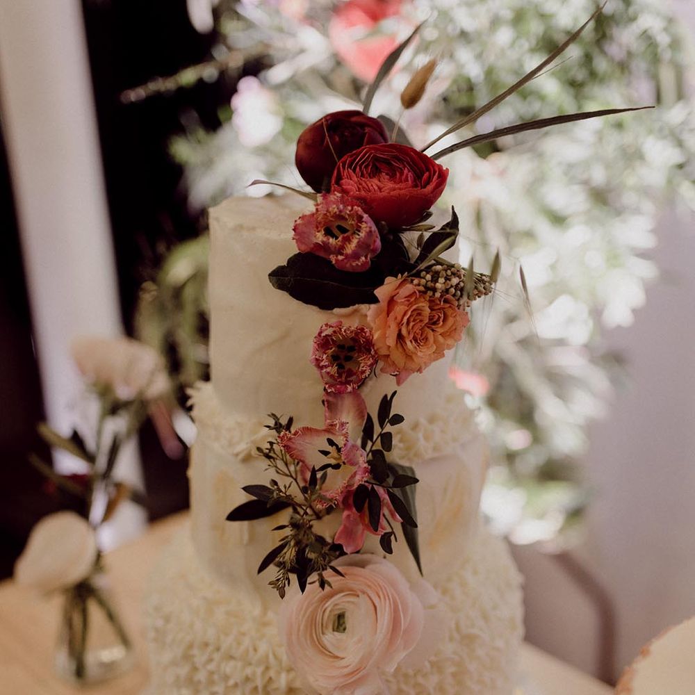 Three tier white frosted wedding cake with icing patterns and decorated with dark flowers
