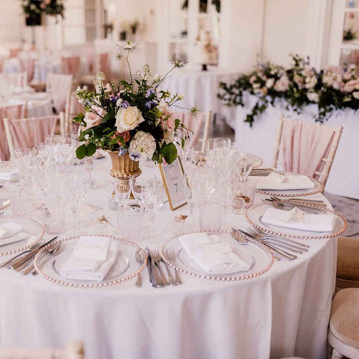 White tablecloths, pink and clear chargers, white rose and colourful flower table centrepiece with chair backs decorated with pink chiffon 