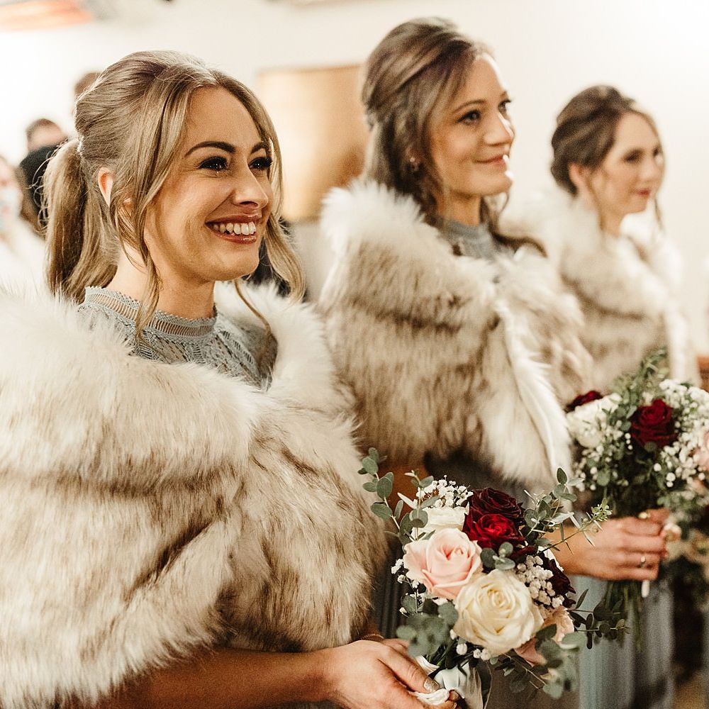 Bridesmaids wear faux fur stoles complete with red and white floral bouquets 