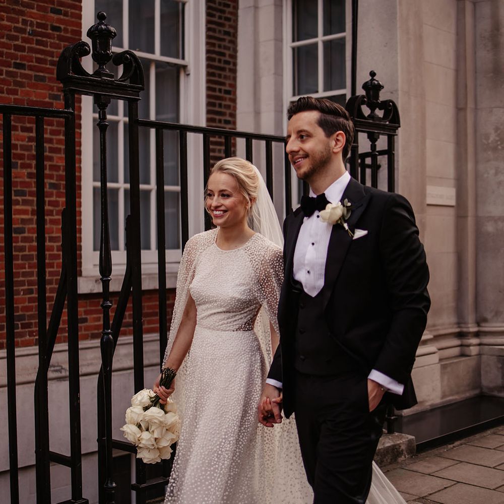 Bride and groom walk along the streets of London with bride in Jesus Peiro cape and groom in black tie 