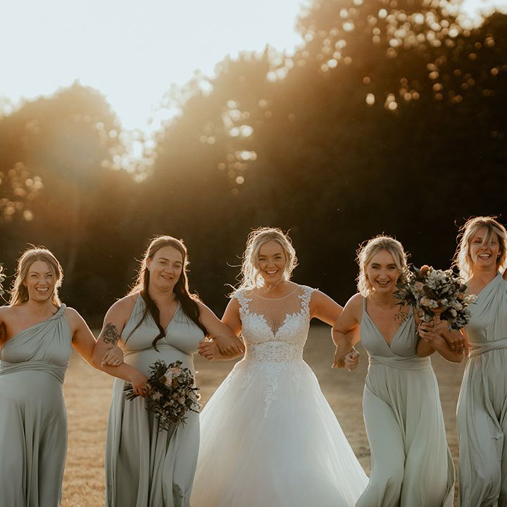 Bridesmaids in sage green dresses in different styles walking with the bride in a princess wedding dress during golden hour 