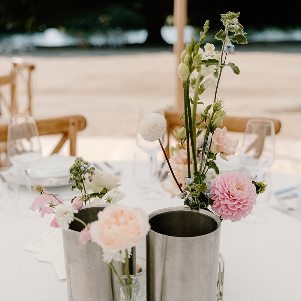 Pastel floral centrepieces in metal vases on rounded tables surrounded by wooden chairs