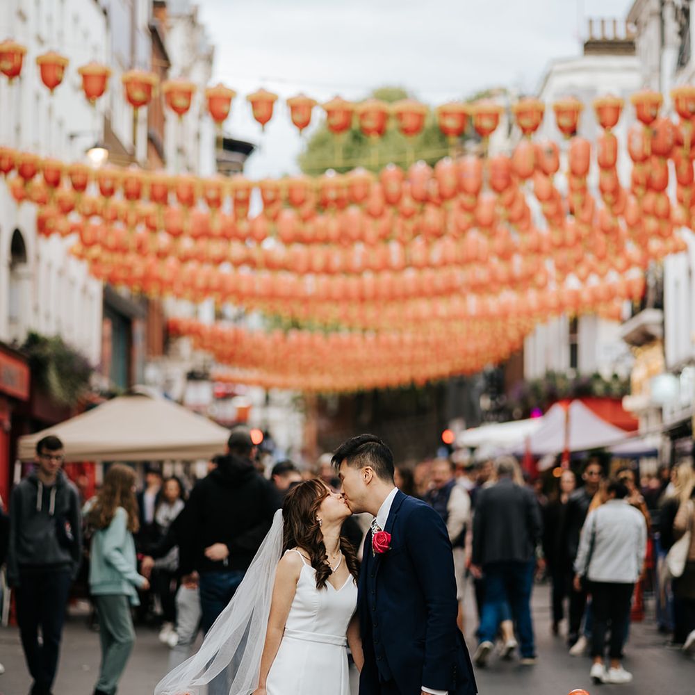 Bride wearing fitted white classic wedding dress kisses her groom in China Town London on their wedding day