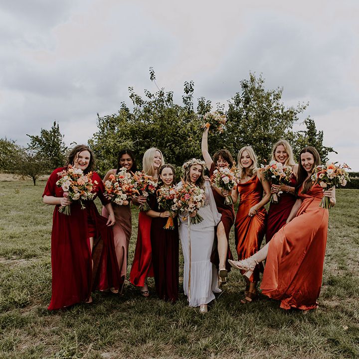 Bride stands with bridesmaids in Autumn colour bridesmaid dresses with boho feel in outdoor wedding photos