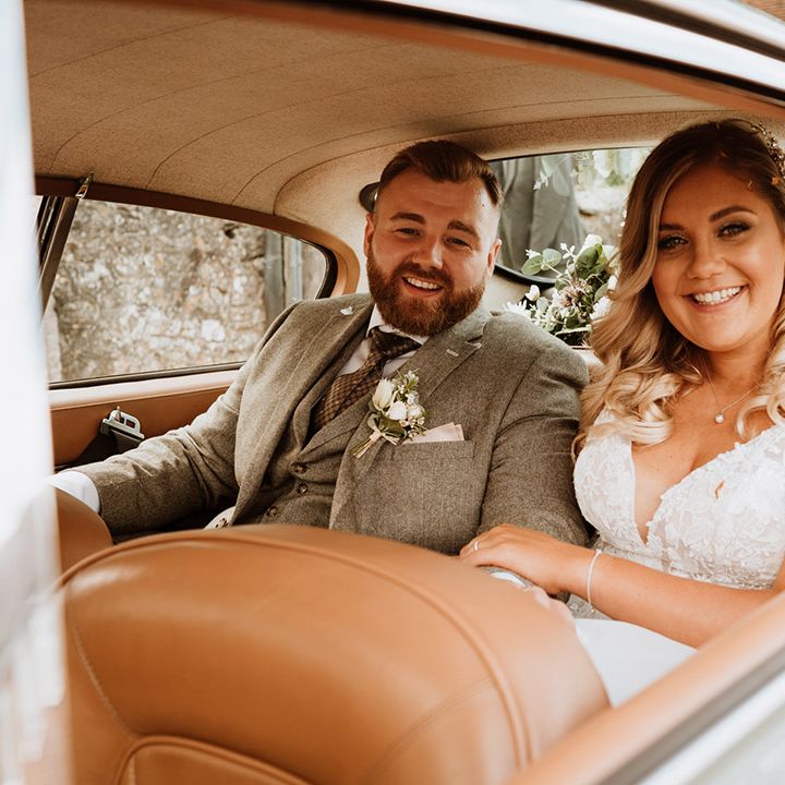 Bride and groom sit in the back of the grey Aston Martin wedding car 