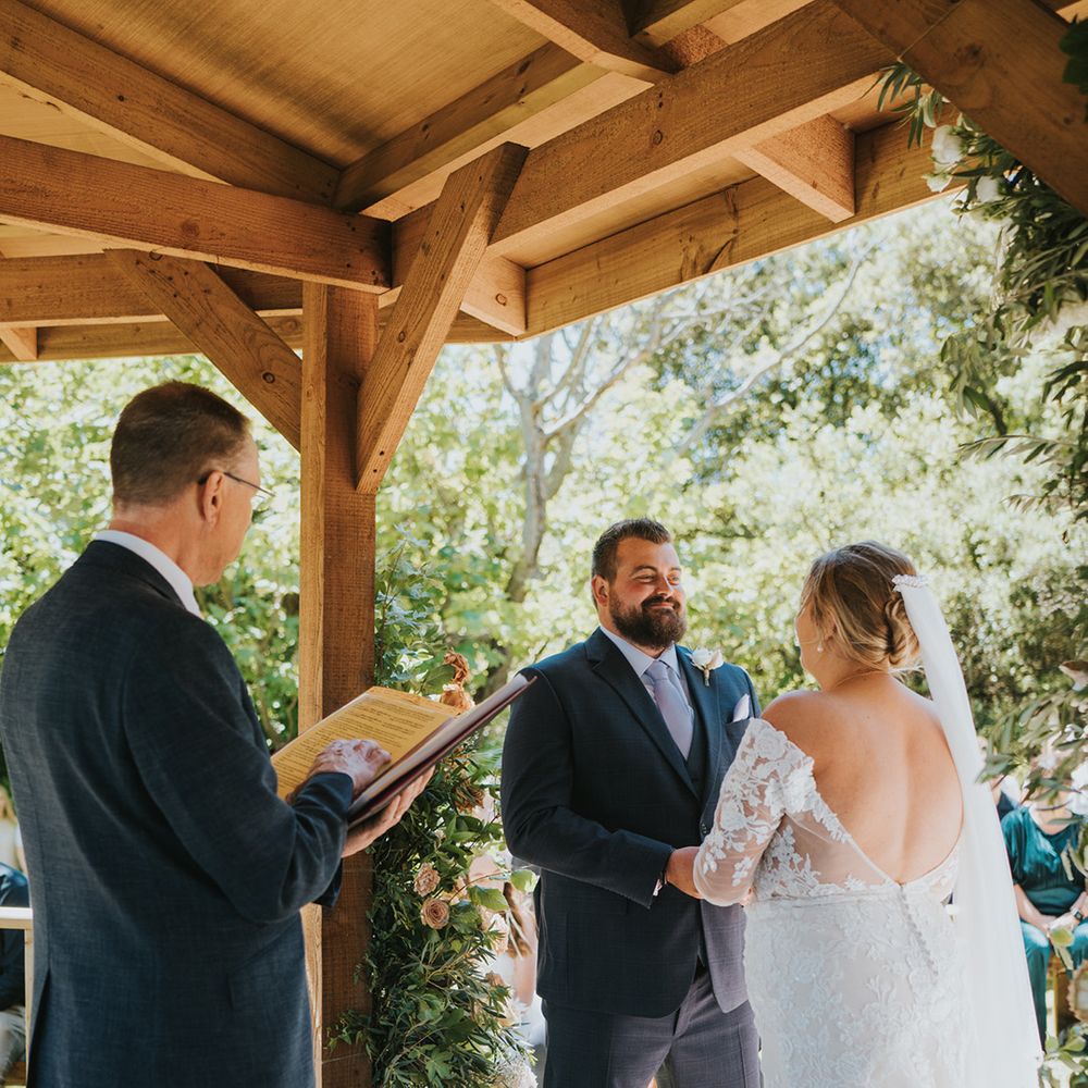 Bride in long sleeve lace wedding dress with low back stands with her groom during outdoor wedding ceremony 