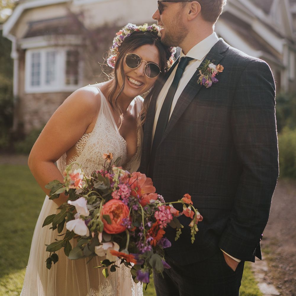 Bride wears colourful flower crown and sunglasses on her wedding day outdoors 