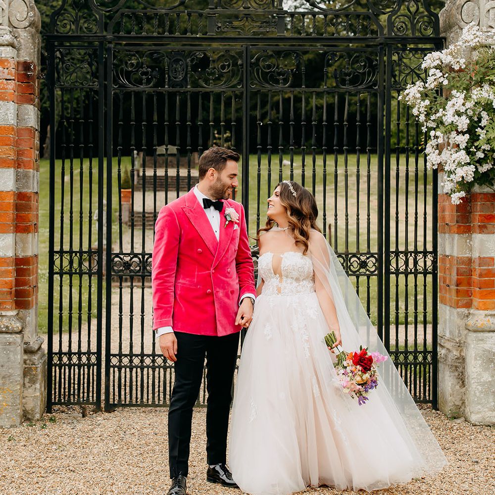 The bride and groom smile at each other as they stand outside the black iron gates at North Mymms Park wedding venue 