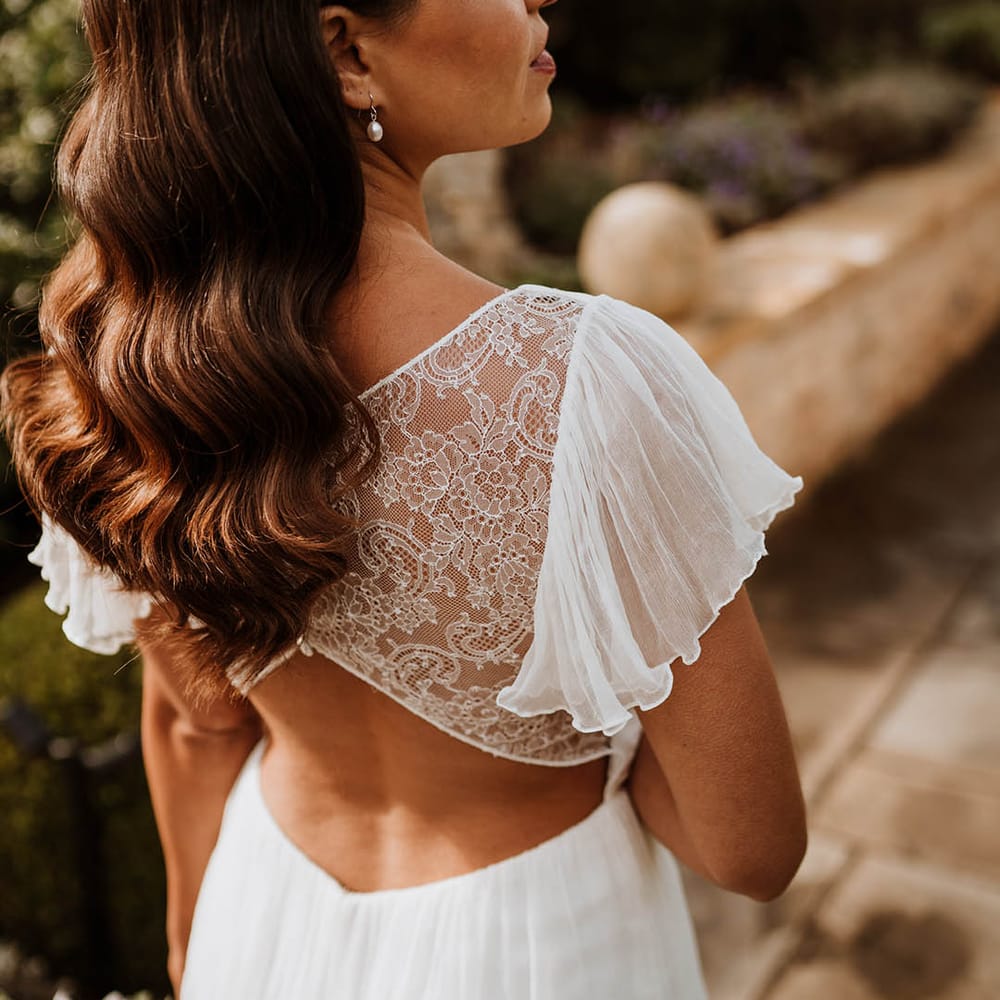 Bride showing open back lace detailing of silk vegan wedding dress and pearl drop earrings