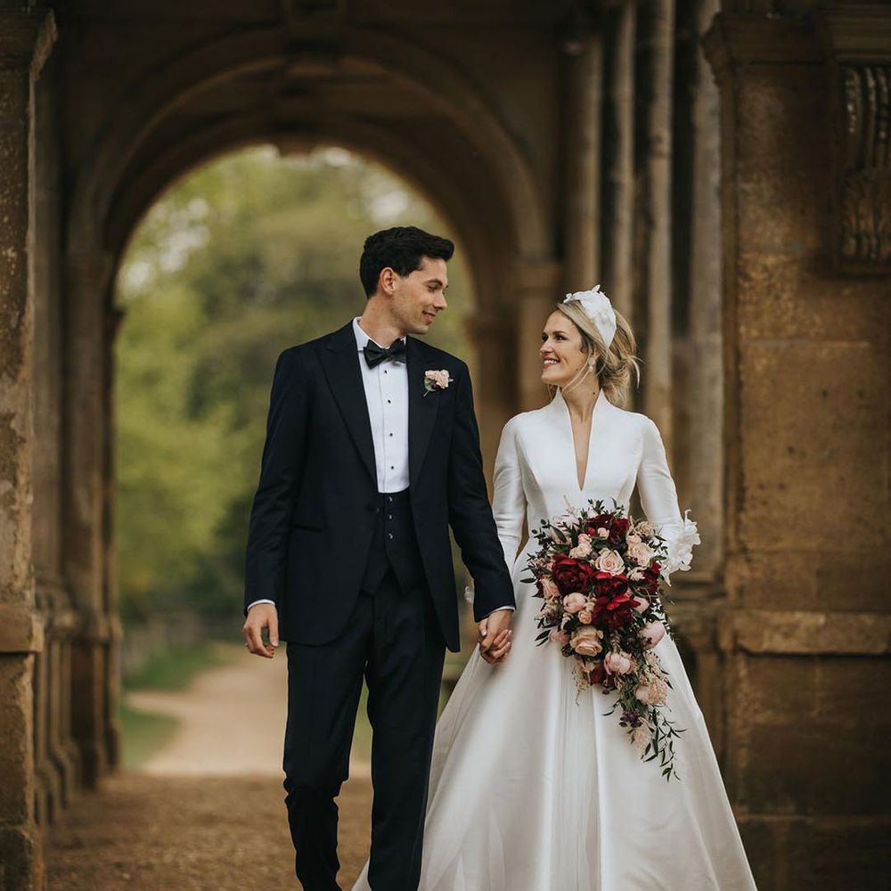 Groom in black tie leads the bride around the gorgeous grounds with the bride in a collared long sleeve wedding dress with sleeve detailing 