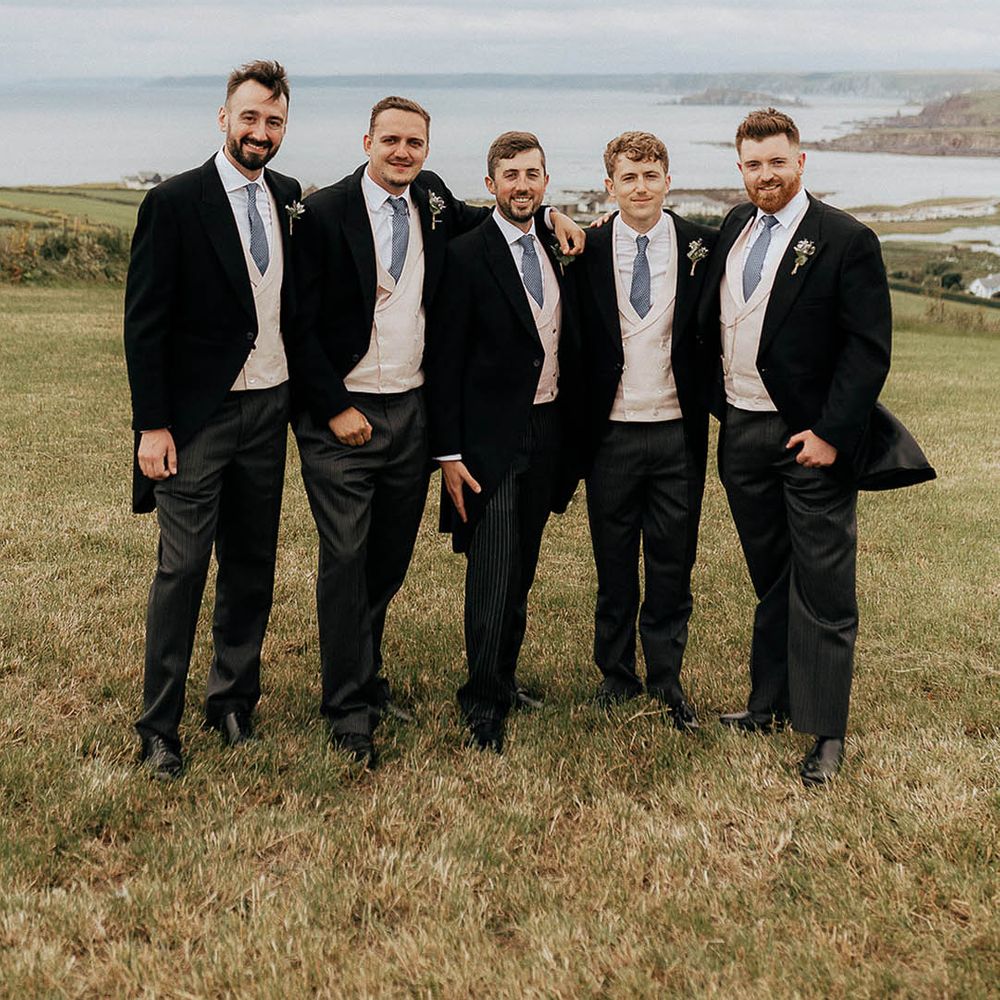 Groom and his groomsmen wear pale pink waistcoats and blue ties with floral buttonholes 