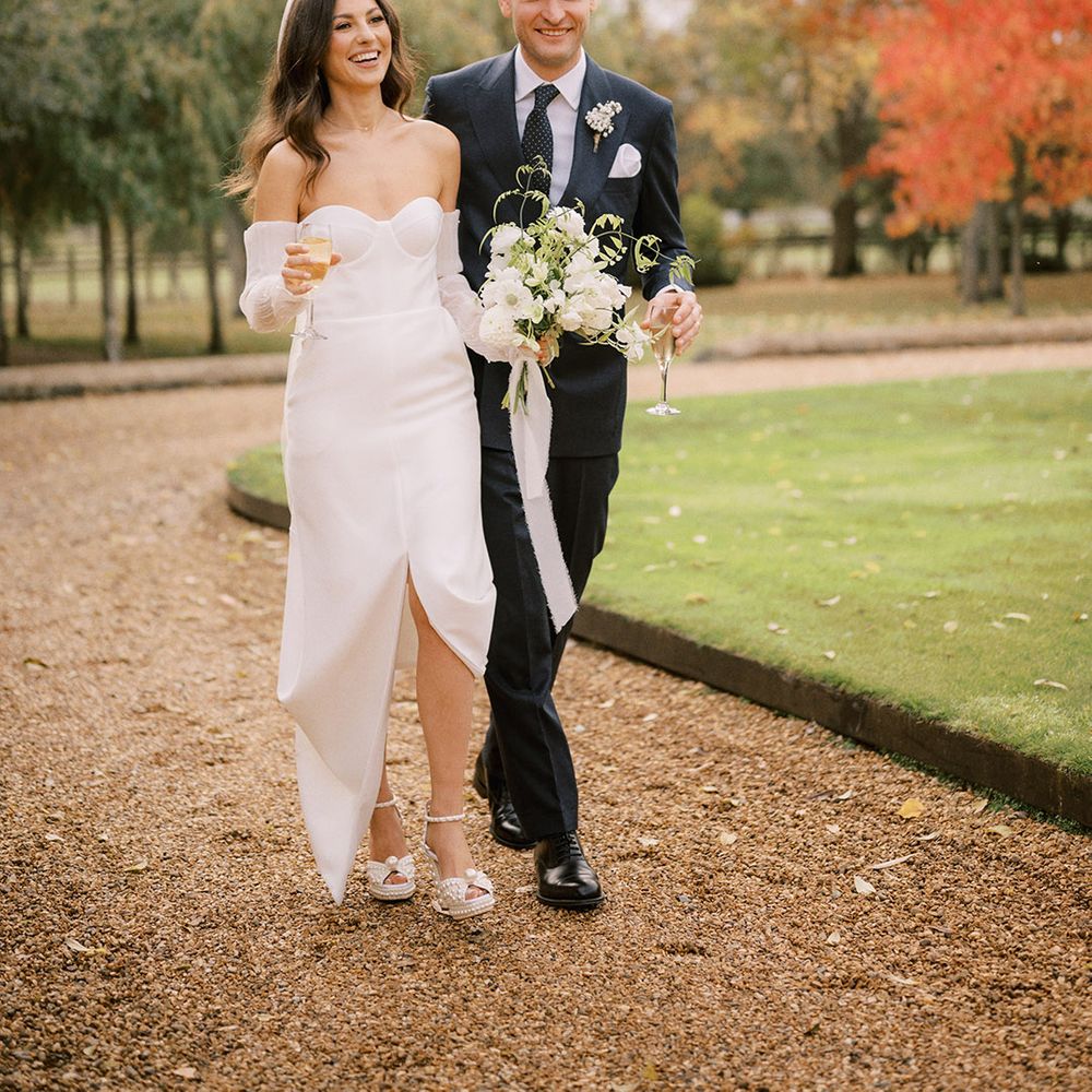 Bride in platform Jimmy Choo pearl shoes wearing a white wedding dress with a split walking with the groom in a navy suit 