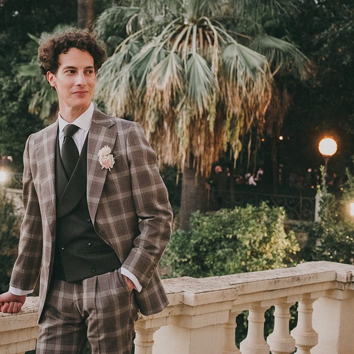 groom with curly hair in a grey check suit and a black double breasted waistcoat 