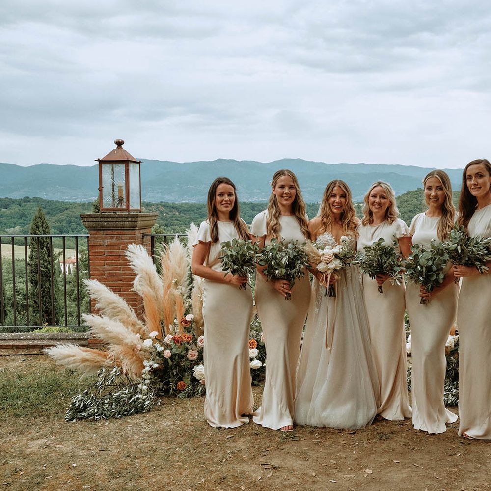 Bridal party pose at altar wearing off white satin bridesmaid dresses in front of pampas grass decor whilst holding eucalyptus bouquets
