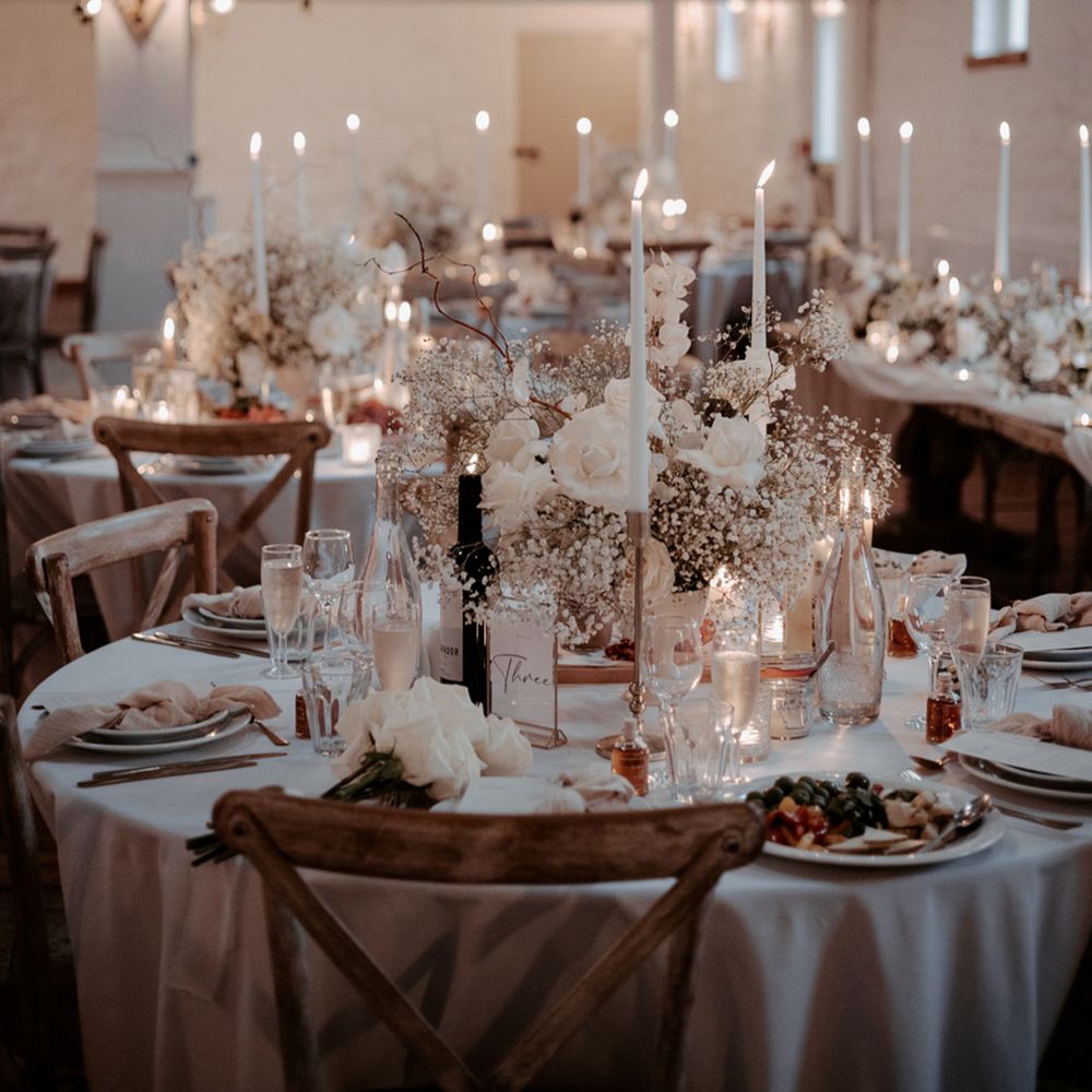 All white wedding tablescape with white rose and gypsophila centrepieces with table name signs and tall taper candles in gold holders 