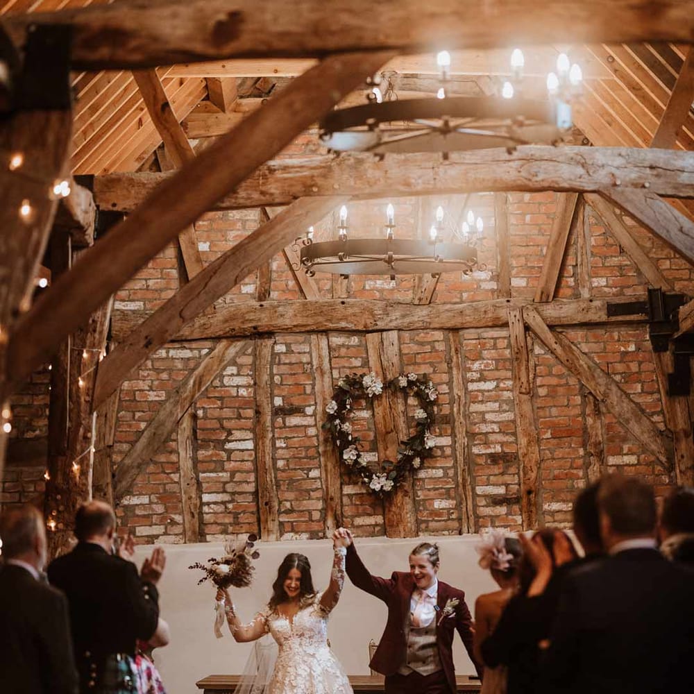 Brides raising their arms and walking out of Bassmead Manor Barns wedding venue to music 