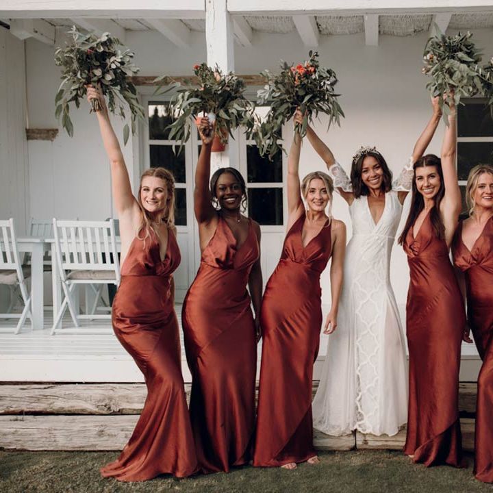 Bride in v neck short cut out sleeve wedding dress posing with bridesmaids in burnt orange bridesmaid dresses 