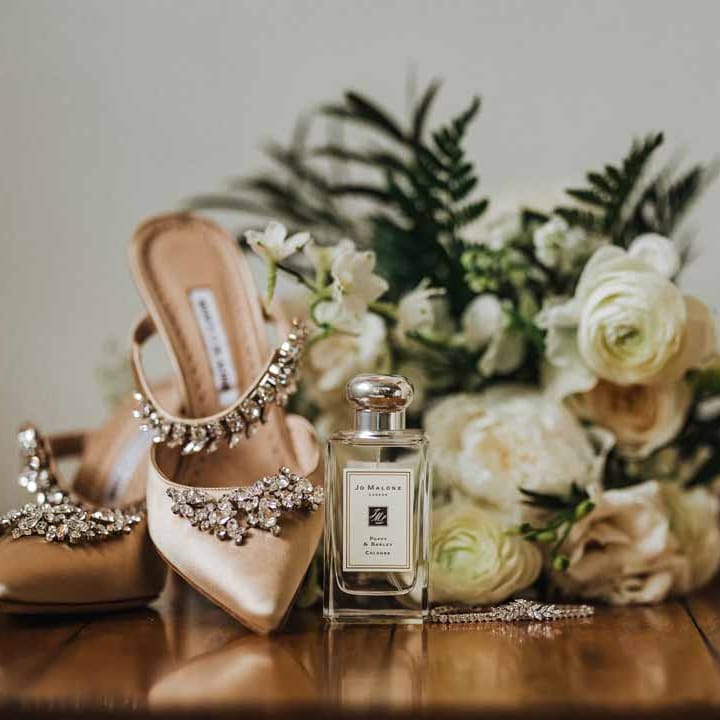 Jo Malone London wedding scent next to light pink bejewelled closed toe wedding heels, silver wedding jewellery and white garden rose, white hydrangea, cows parsley and foliage bridal bouquet 