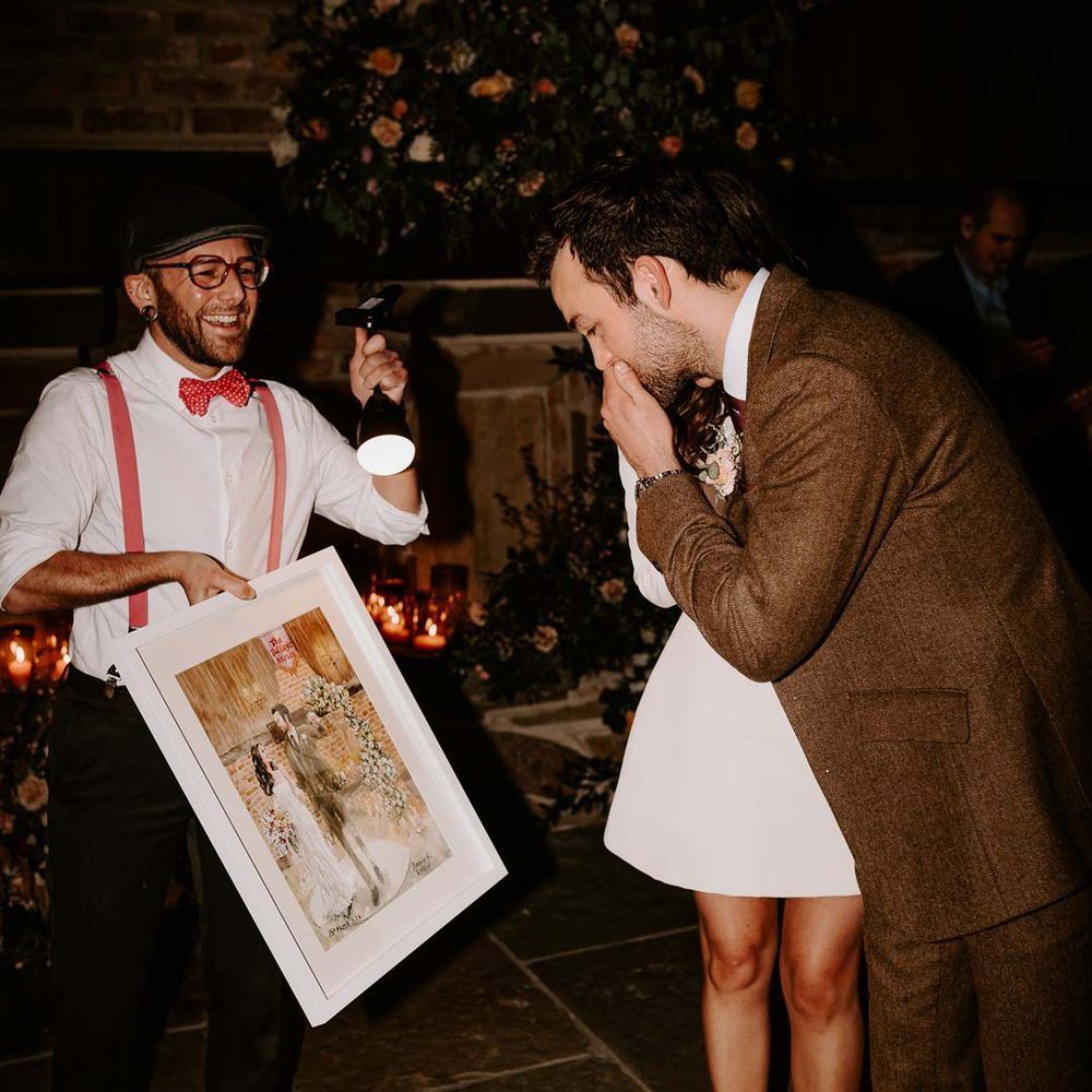 Bride in long sleeve short wedding dress and red velvet chunky wedding heels and groom in brown grooms suit reacting to live wedding painting 