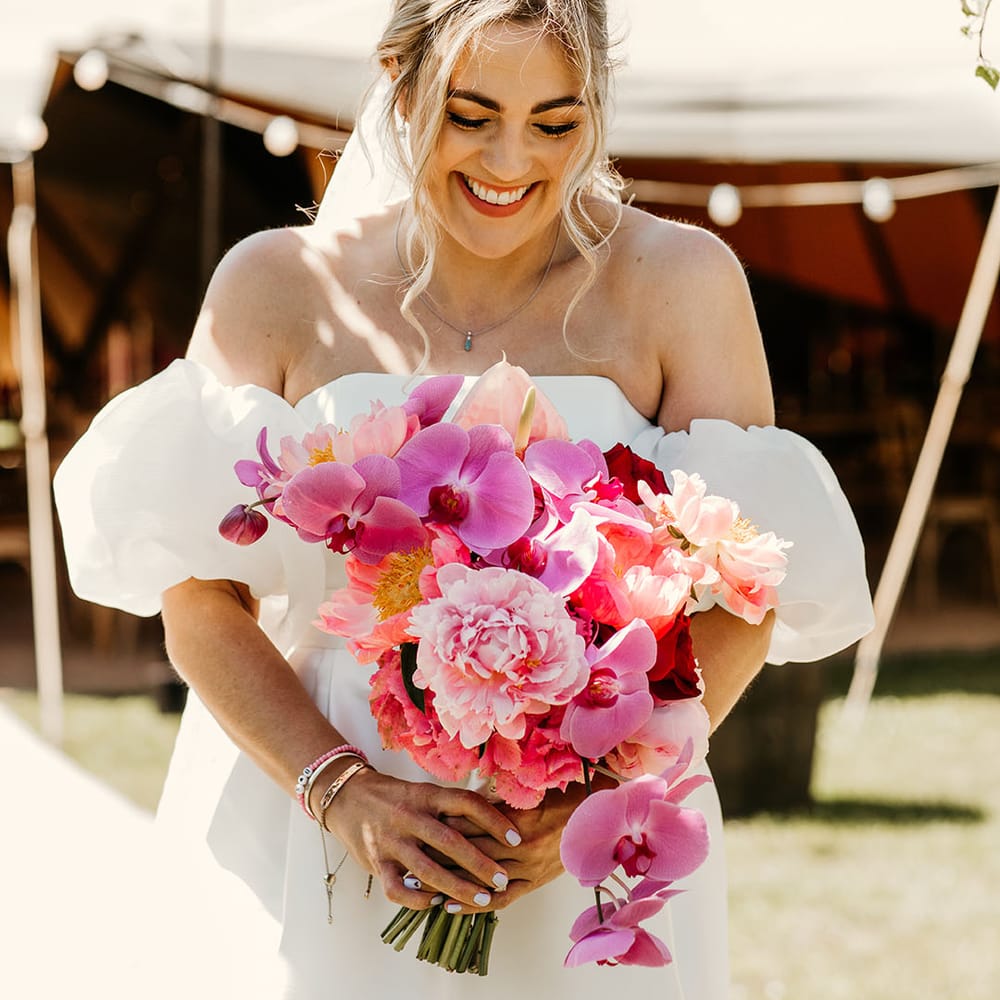 Laughing bride holding bright pink bouquet with orchids and roses 