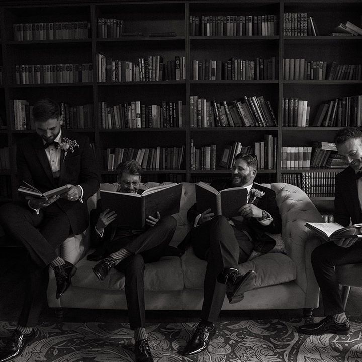 Groomsmen pose together in the morning as they get ready for the wedding reading books 