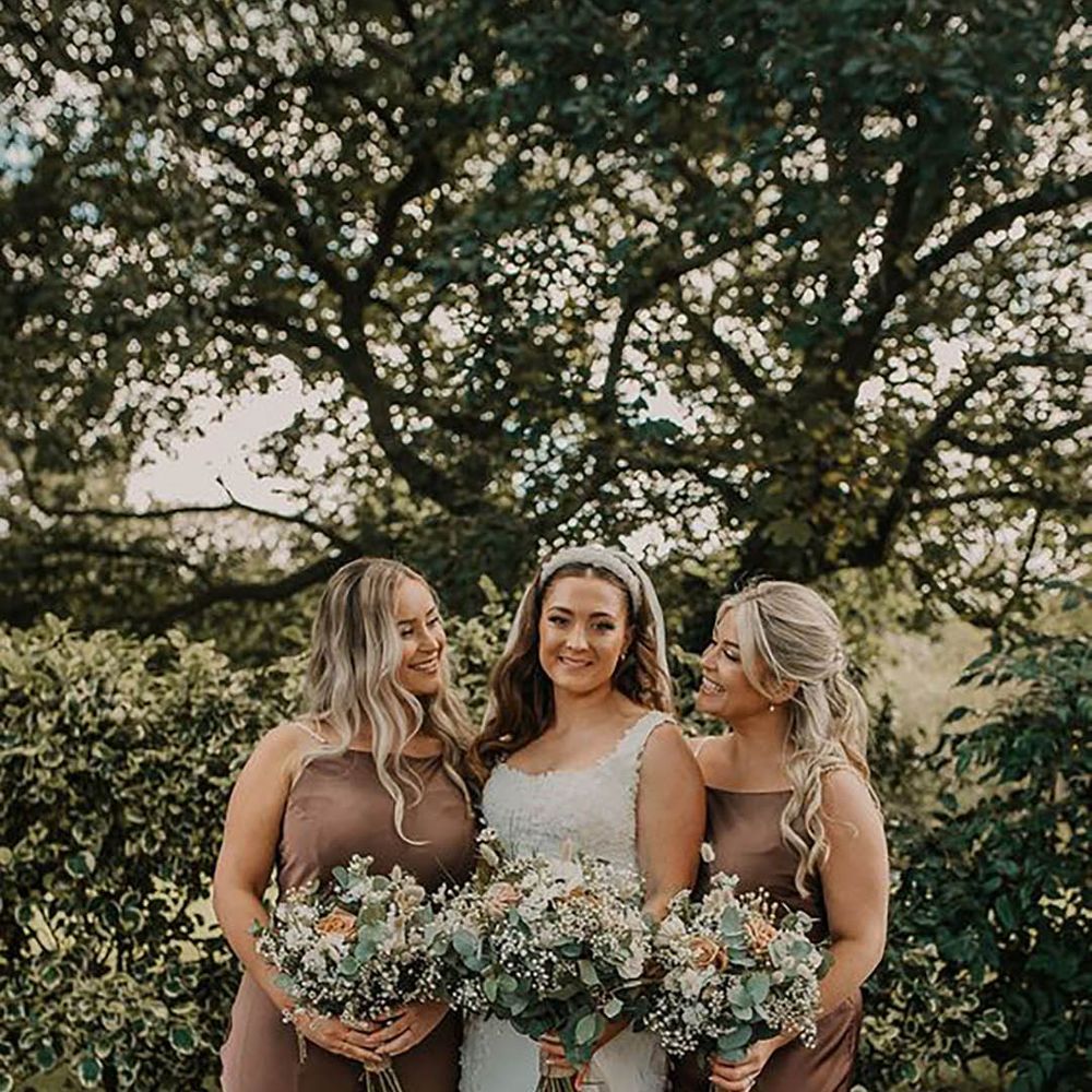 Bride smiling for a picture with two bridesmaids wearing brown bridesmaid dresses by Pink Wave Photography 