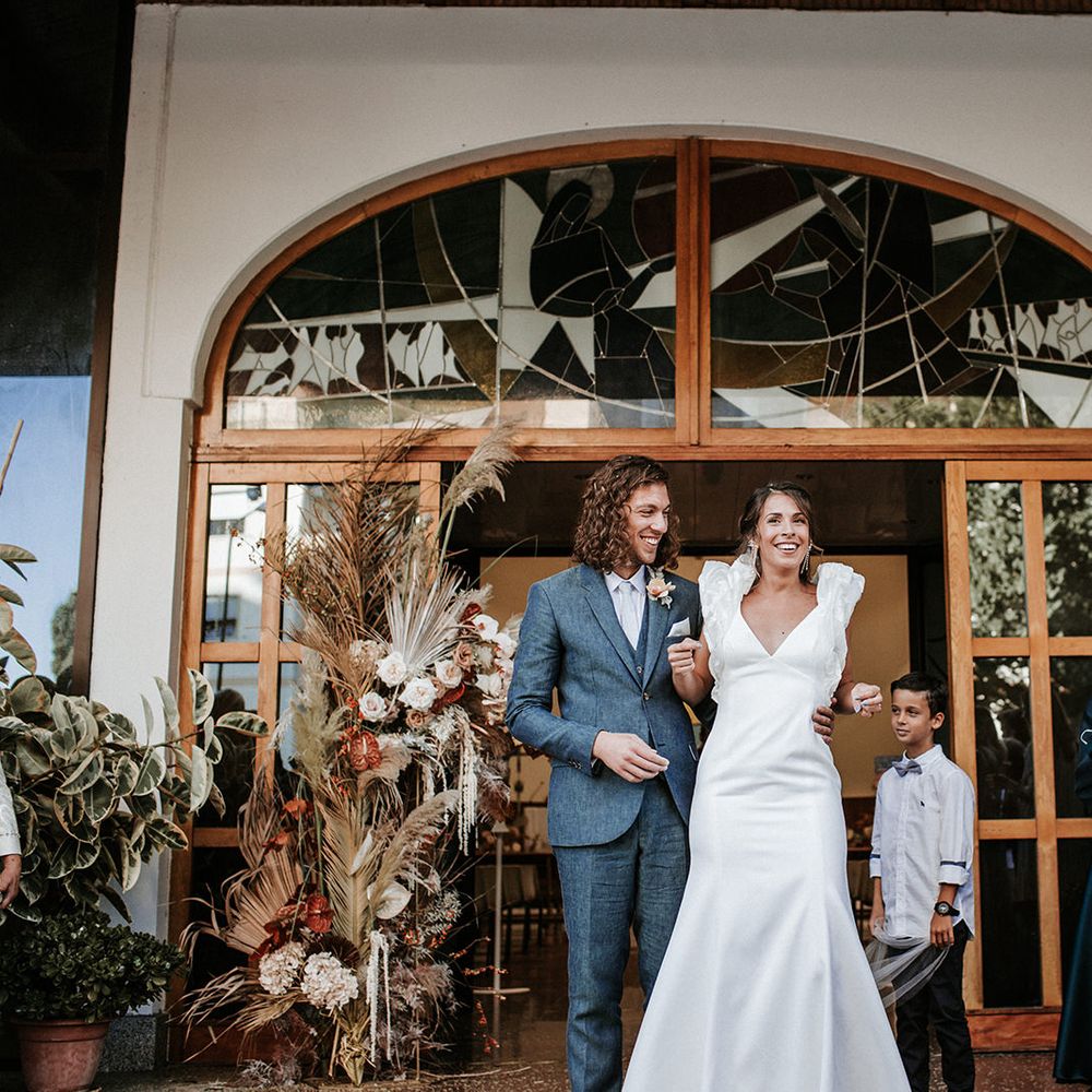 Bride and groom exit their wedding ceremony in a navy suit and ruffle sleeve wedding dress