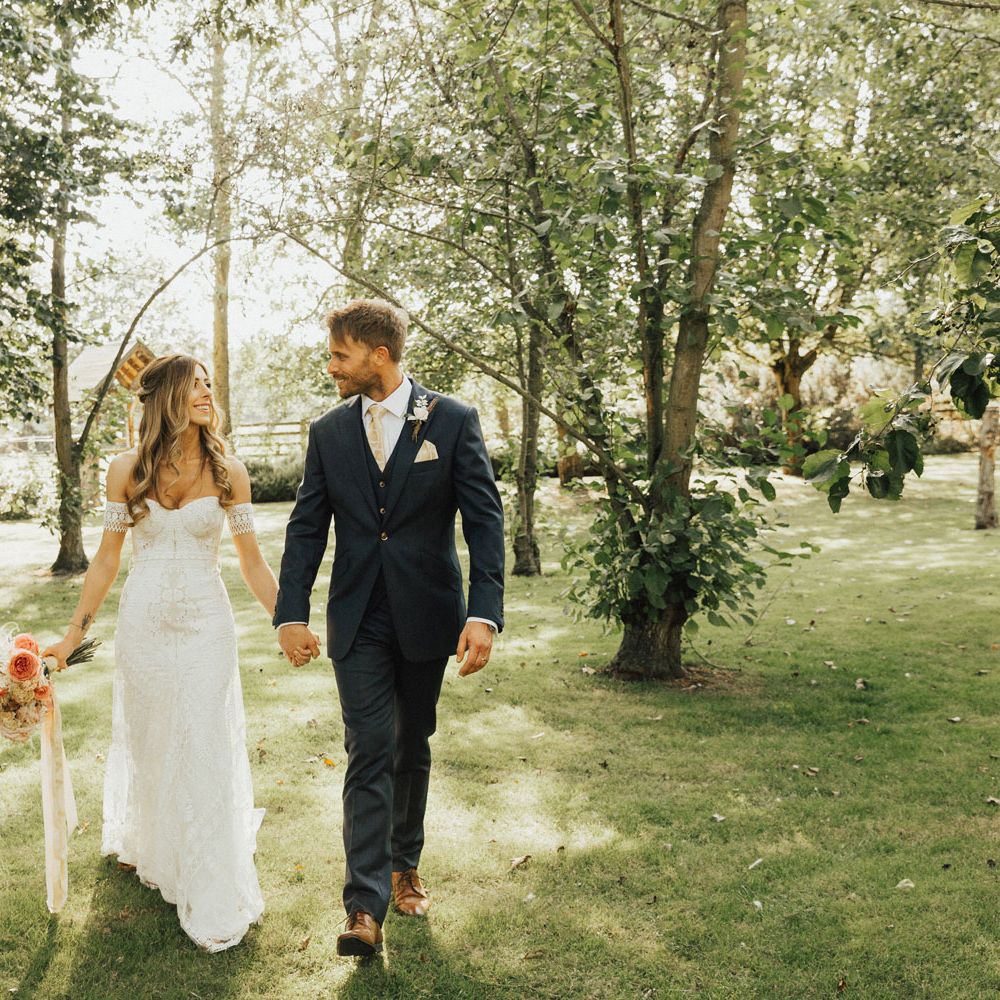 Bride in Clara Rue De Seine wedding dress holds hands with groom walking in gardens at Tythe Barn Wedding