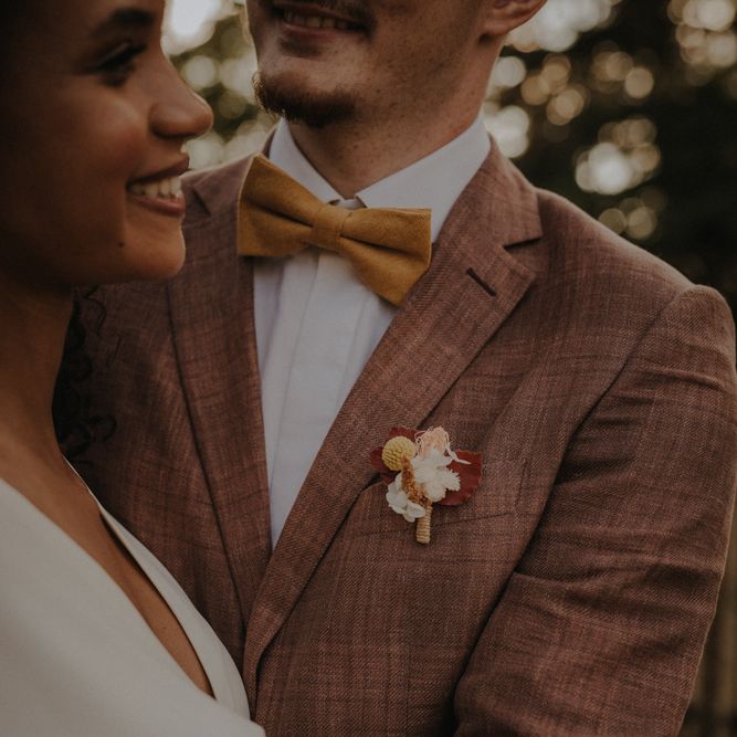 Groom in a brown check wedding suit and orange bow tie with a delicate buttonhole flower