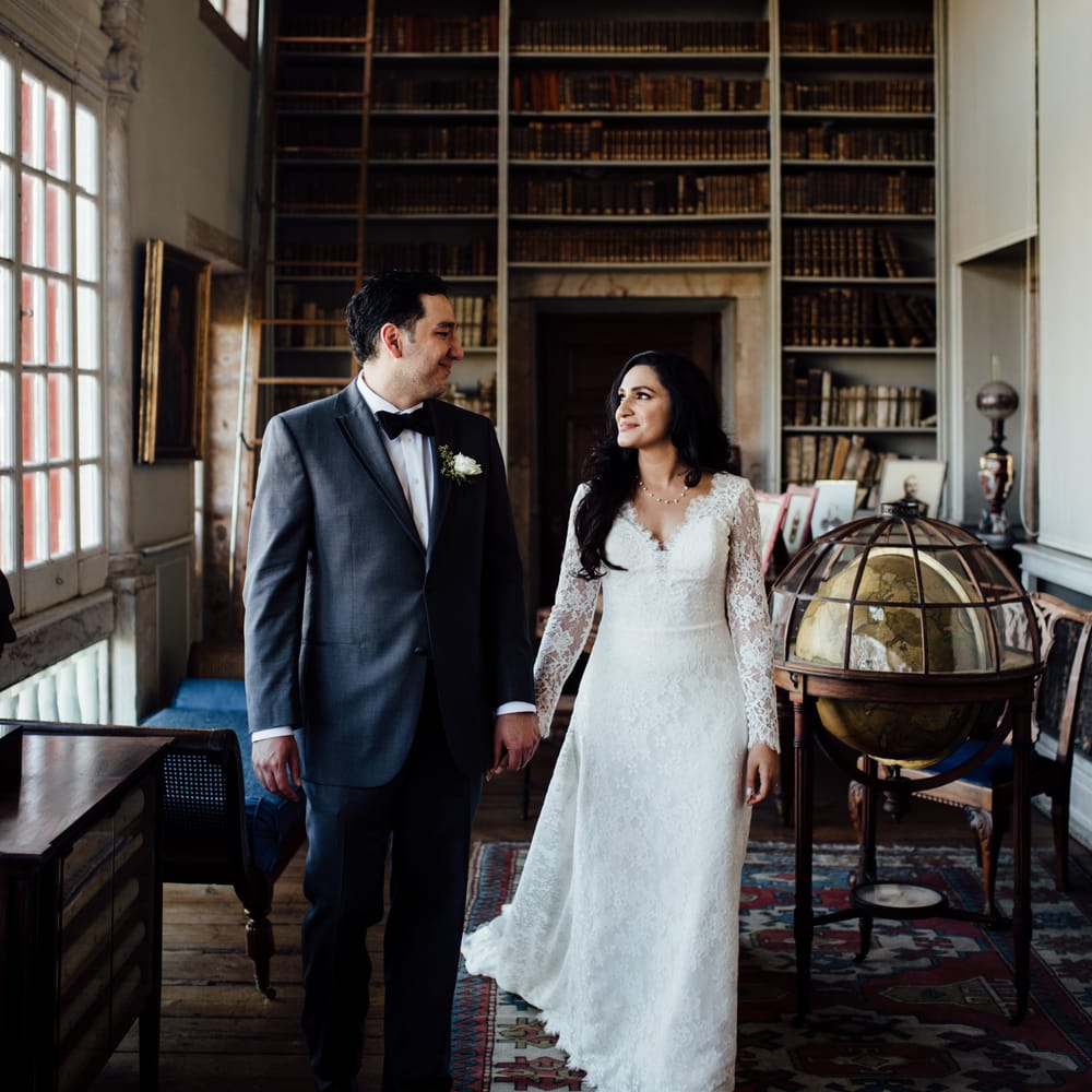 Bride & groom look lovingly at one another in front of bookcase 