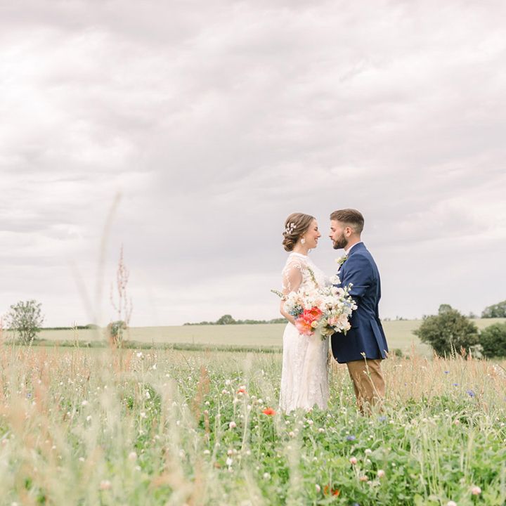 Romantic bride and groom portrait in a field with the bride in a lace wedding dress and the groom a blue jacket 