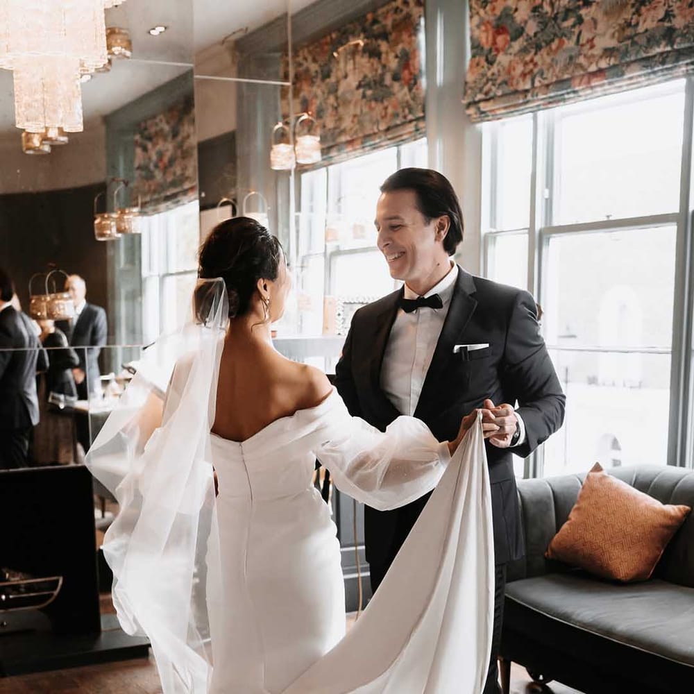 Brides long wedding dress is held up whilst she dances with Groom in dark tailored suit 
