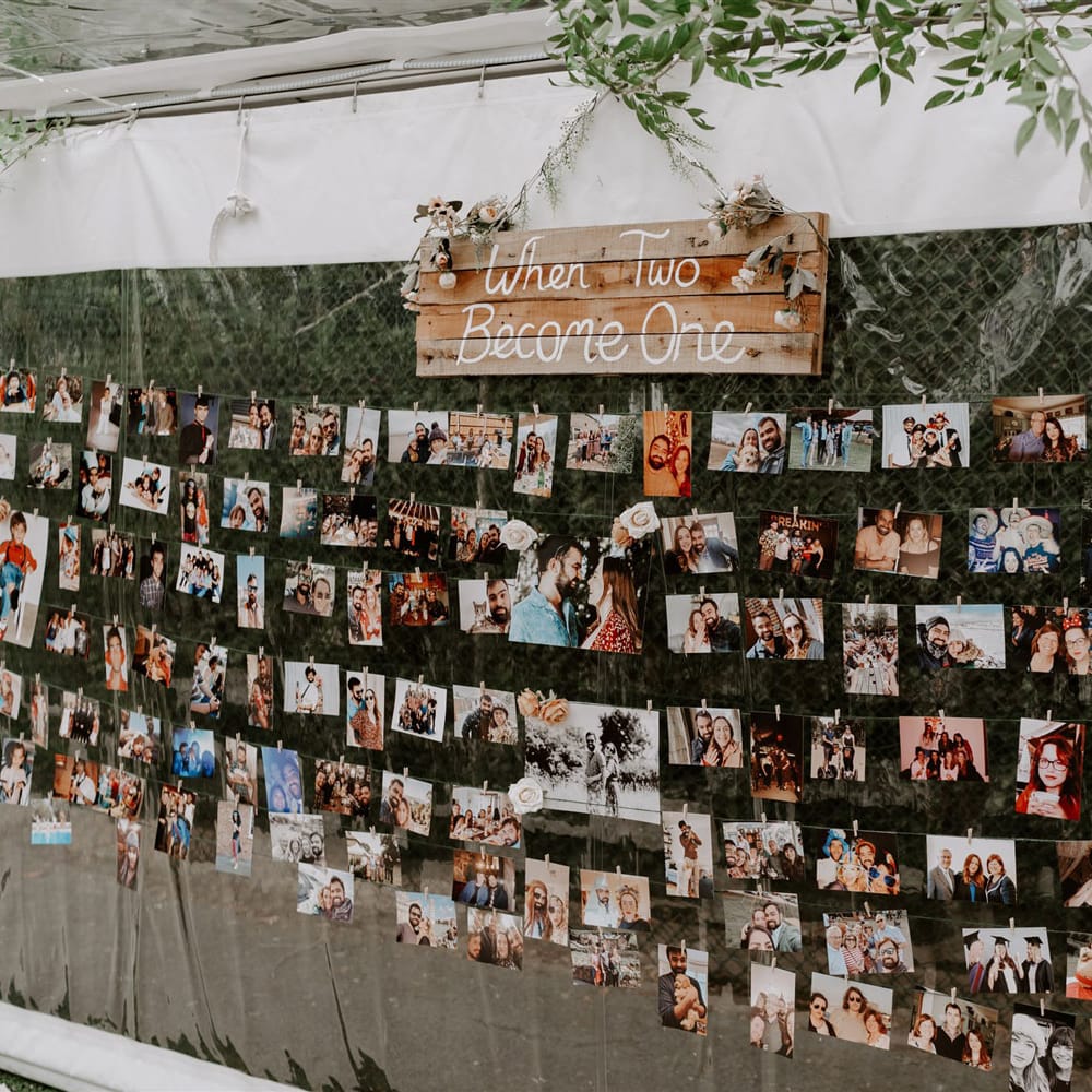Various photos pegged to string across interior side of marquee with wooden wedding sign reading 'when two became one'