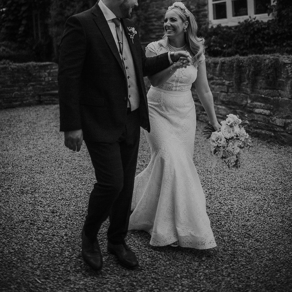 Black and white picture of the bride in a lace wedding dress and groom in a three piece suit holding hands at their Dewsall Court wedding 
