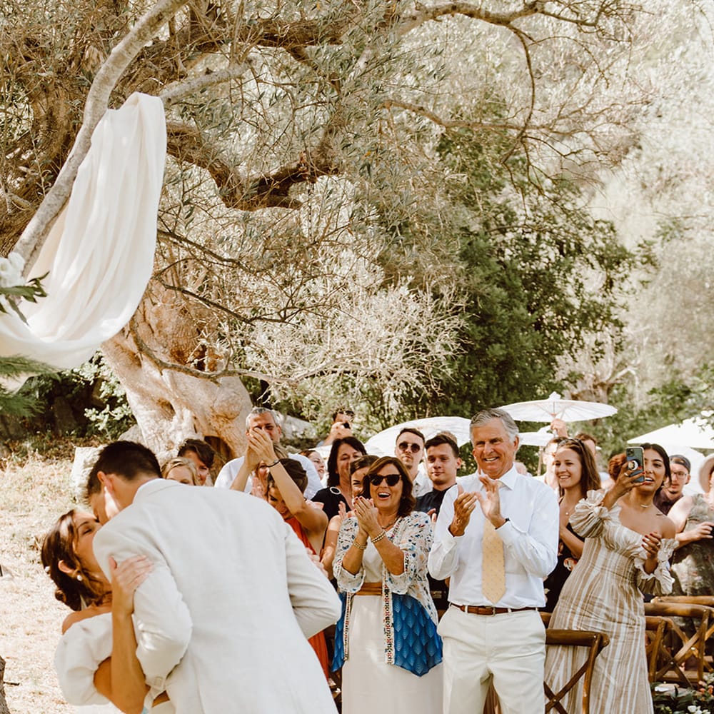 Wedding guests applaud as bride and groom share their first kiss as a married couple